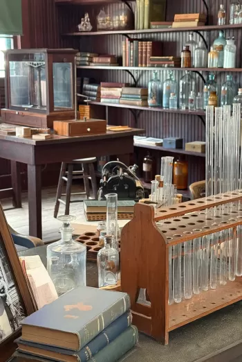 Interior of Edison and Ford Winter Estates laboratory displaying antique wooden tables, glass bottles, test tubes, and vintage books with an overlay praising the museum.
